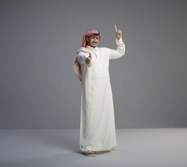 رجل سعودي بالزي التقليدي يشير للأعلى بابتسامة واثقة