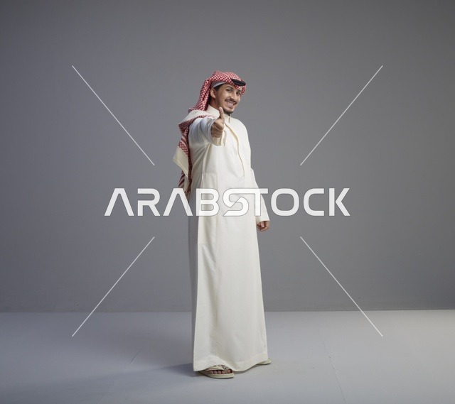 رجل سعودي بالزي التقليدي يشير بالإبهام داخل استوديو