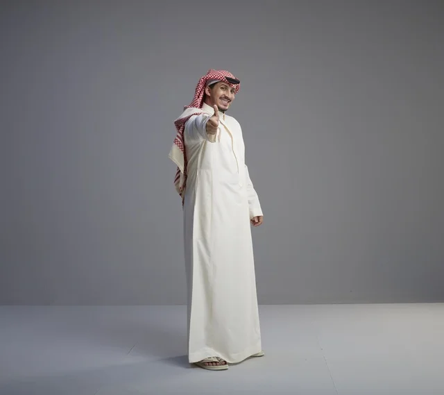 رجل سعودي بالزي التقليدي يشير بالإبهام داخل استوديو