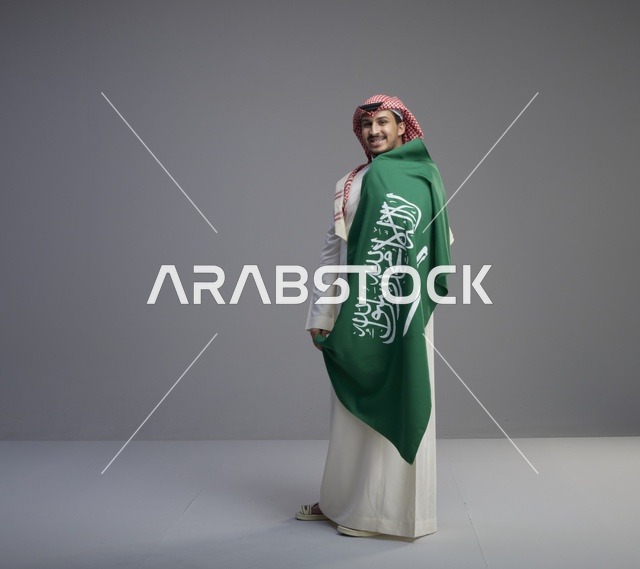 رجل سعودي بالثوب التقليدي يحمل العلم الوطني السعودي