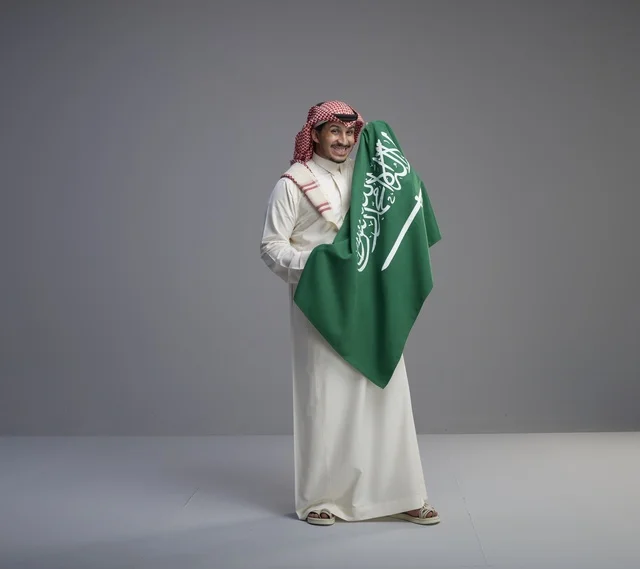 رجل سعودي يحمل العلم الوطني بالزي التقليدي