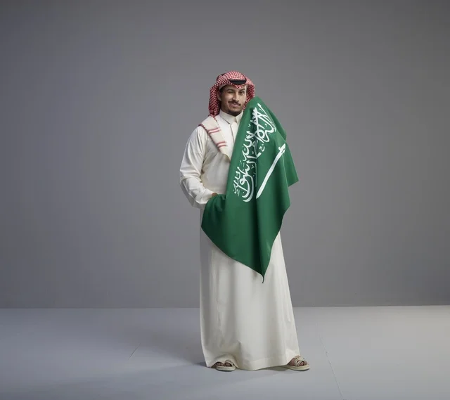 رجل سعودي بالزي التقليدي يحمل العلم الوطني