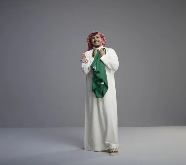 رجل سعودي يحمل العلم الوطني بالثوب التقليدي في استوديو