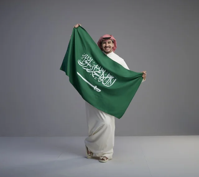 رجل سعودي مبتسم يحمل العلم الوطني في استوديو تصوير