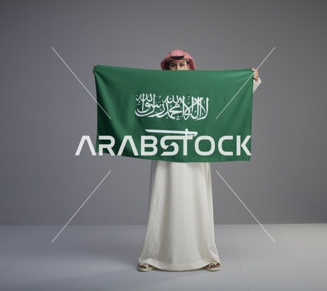 رجل سعودي يرتدي الثوب ويحمل العلم الوطني السعودي