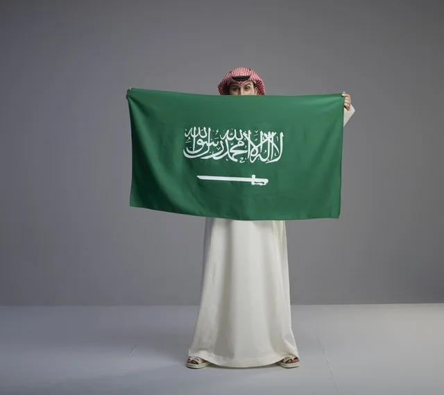 رجل سعودي يرتدي الثوب ويحمل العلم الوطني السعودي