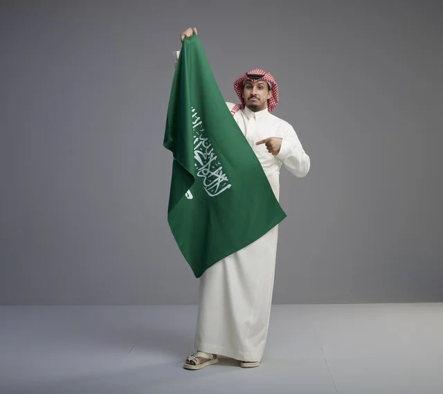 رجل سعودي يحمل العلم الوطني السعودي بخلفية رمادية