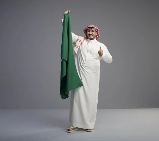 رجل سعودي يبتسم ويحمل العلم الوطني السعودي في الاستوديو