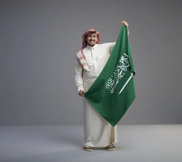 رجل سعودي يحمل العلم الوطني بالثوب التقليدي