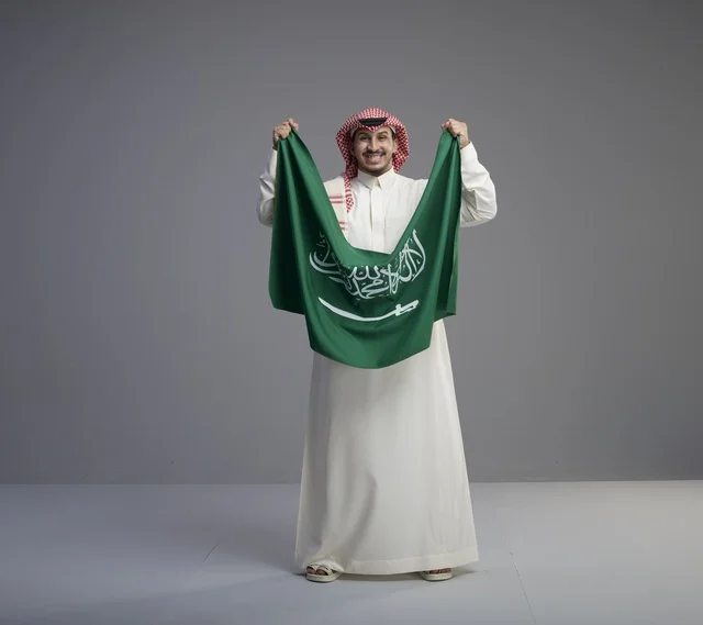 رجل سعودي يحمل العلم الوطني السعودي بالزي التقليدي