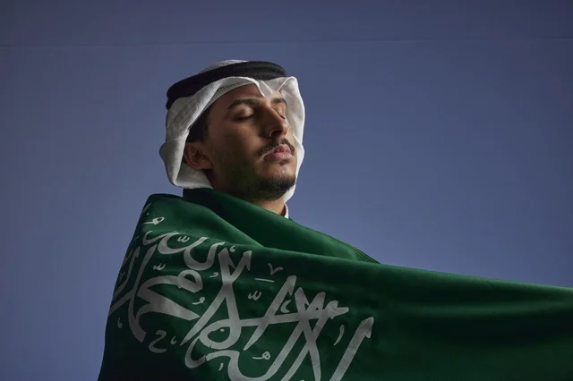 شاب سعودي يلتف بالعلم السعودي بفخر واعتزاز