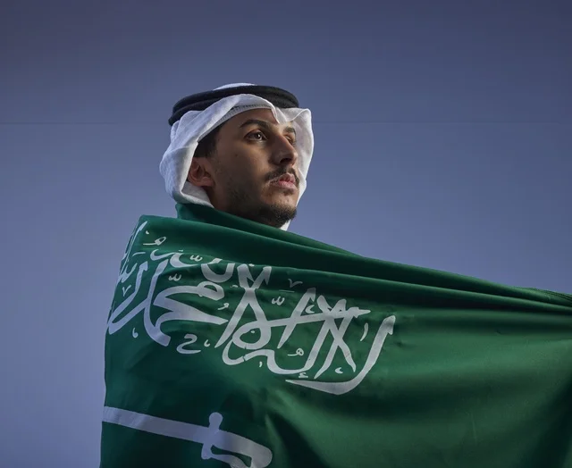 Saudi Man Wrapped in National Flag Under Blue Sky