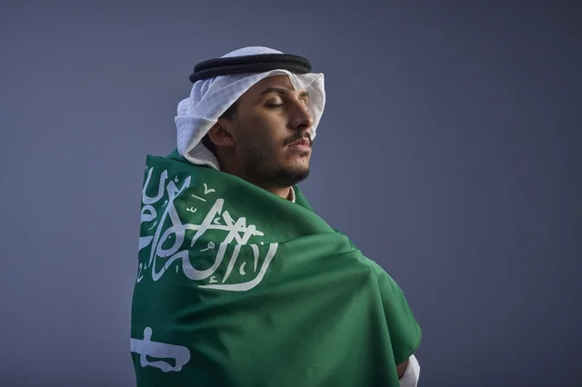 شاب سعودي يلتف بالعلم الوطني السعودي في الاستوديو