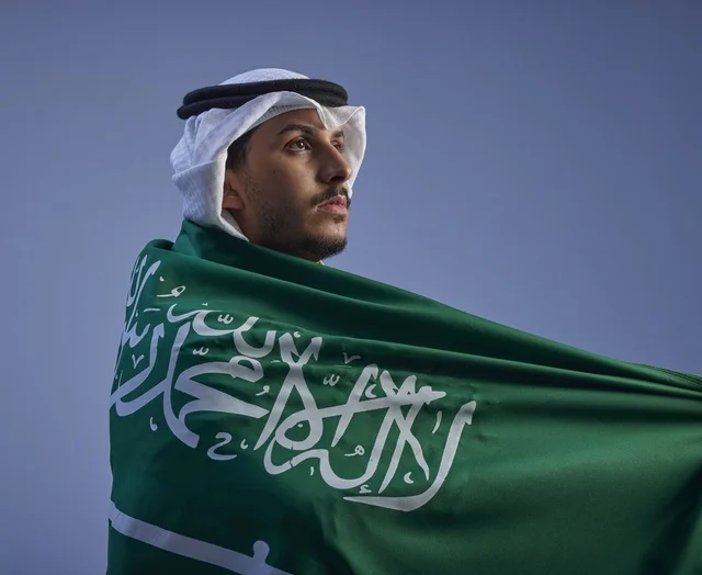Saudi Man Wrapped in National Flag Under Blue Sky