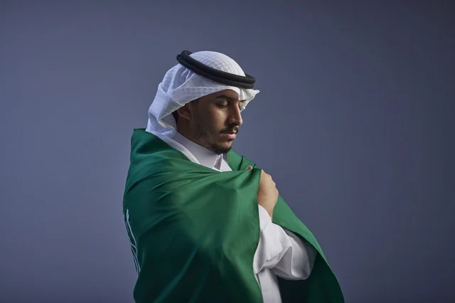 شاب سعودي يرتدي الزي التقليدي ويلتف بالعلم الوطني