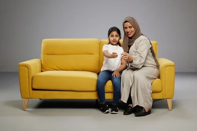 Saudi Mother and Daughter Holding Blank Card on Sofa