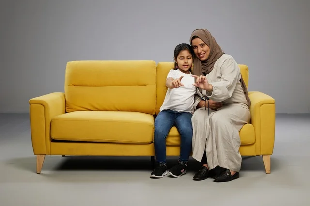 Saudi Mother and Daughter with Blank Card on Yellow Sofa