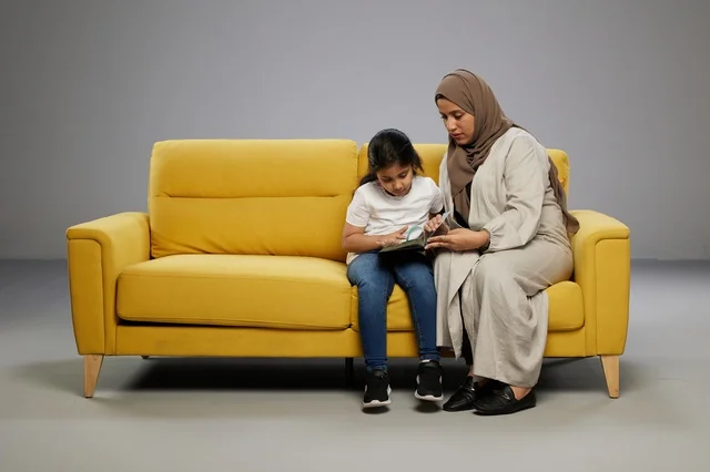 Saudi Mother Reading Book With Daughter on Yellow Sofa