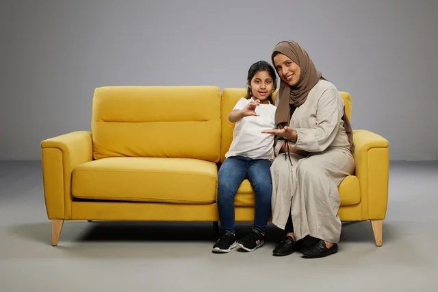 Saudi Mother and Daughter Holding Blank Card on Sofa