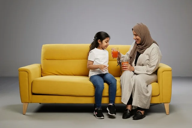 Saudi Mother and Daughter Drinking Juice on Yellow Sofa
