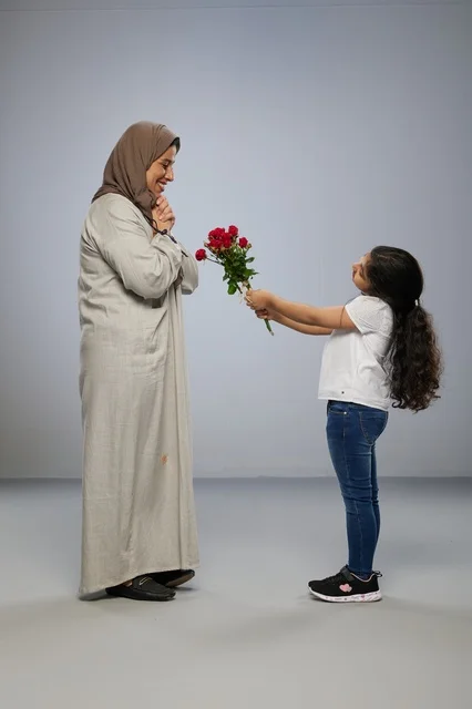 طفلة عربية تقدم زهور حمراء لوالدتها في الاستوديو