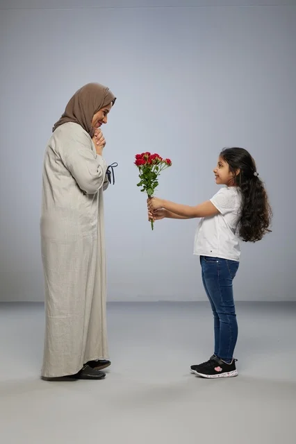 طفلة عربية تقدم زهور حمراء لوالدتها المحجبة