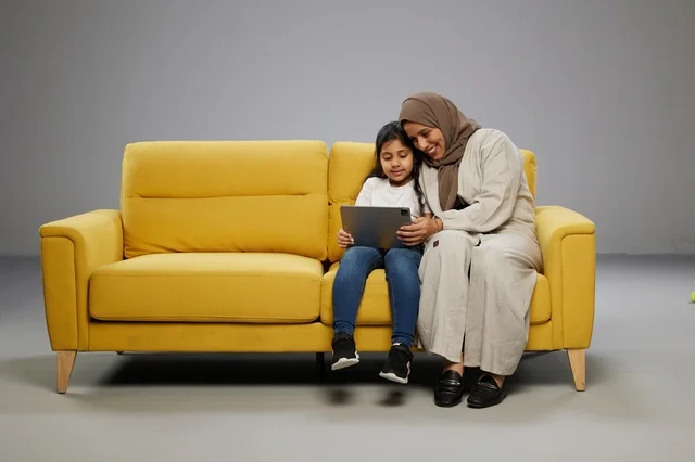 Saudi Mother and Daughter Using Tablet on Yellow Sofa