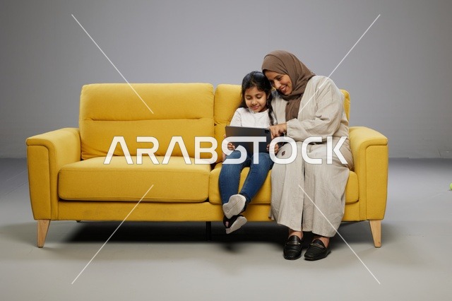 أم وابنتها تستخدمان جهاز لوحي على أريكة صفراء