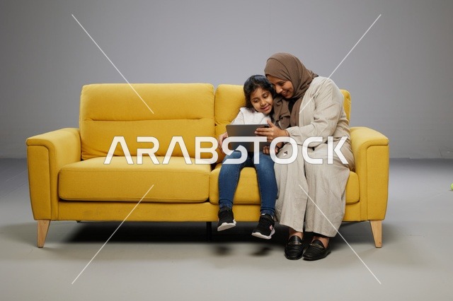 أم وابنتها تستخدمان جهازاً لوحياً على أريكة صفراء
