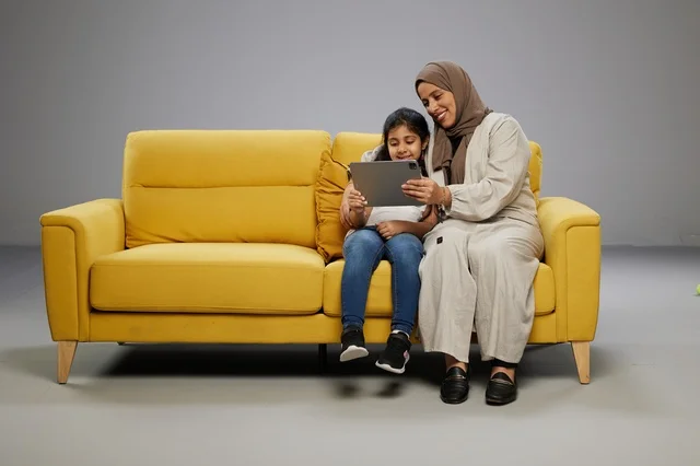 Saudi Mother and Daughter Using Tablet on Yellow Sofa