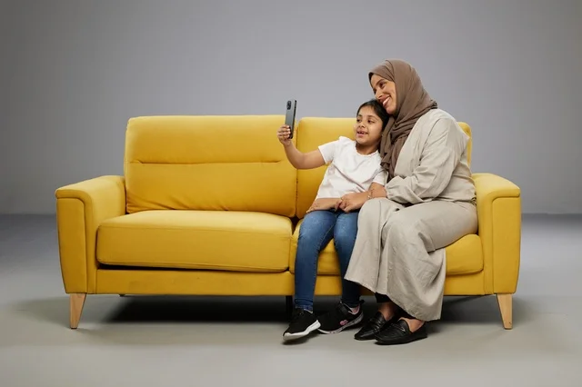 أم وابنتها تلتقطان سيلفي على أريكة صفراء