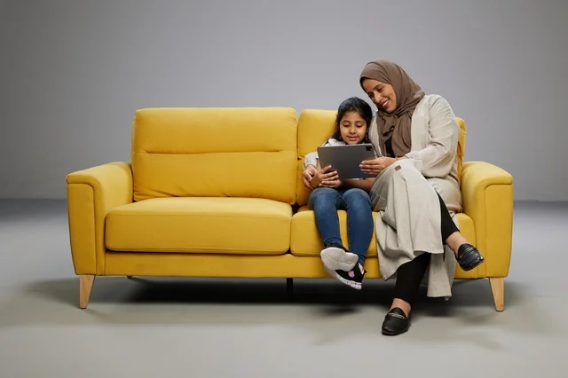 Saudi Mother and Daughter Using Tablet on Yellow Sofa