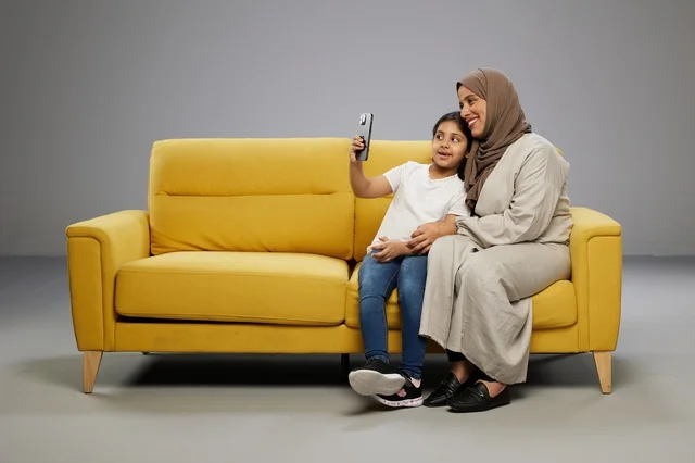 أم وابنتها تلتقطان صورة سيلفي على أريكة صفراء