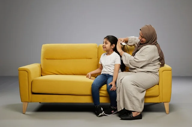 Saudi Mother Brushing Daughter Hair on Yellow Sofa