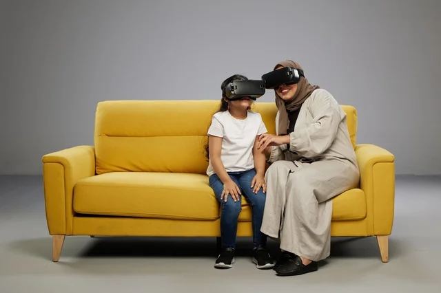 Arab Mother and Daughter Using VR Headsets on Sofa