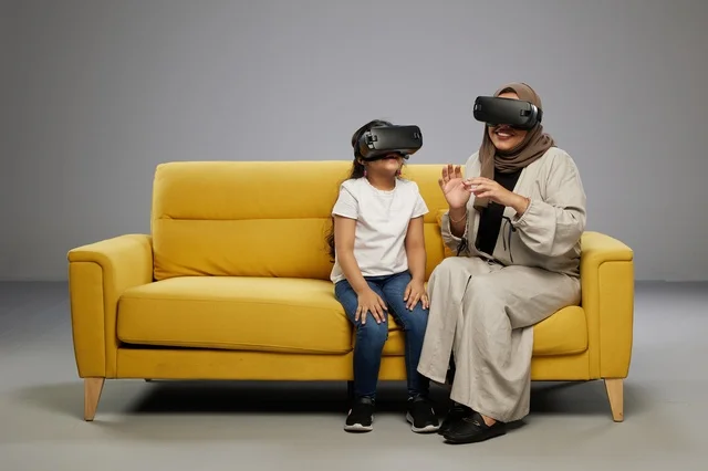 Arab Mother and Daughter Using VR Headsets on Sofa