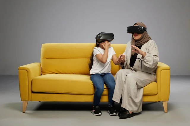 Saudi Mother and Daughter with VR Headsets on Sofa