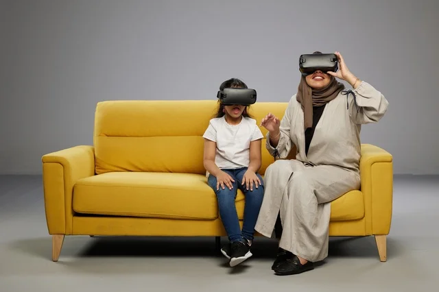 Saudi Mother and Daughter Using VR Headsets on Sofa