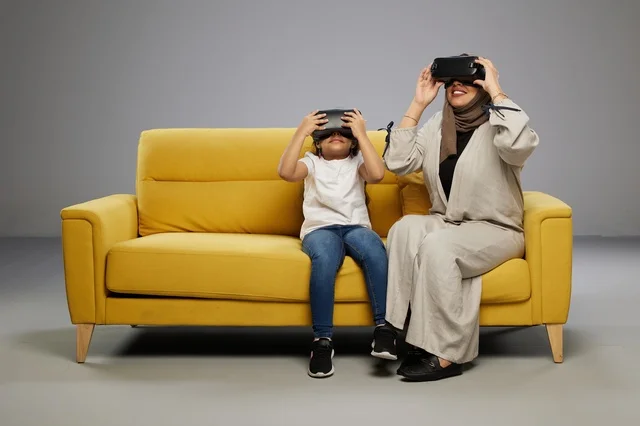 Saudi Mother and Daughter Using VR Headsets on Sofa