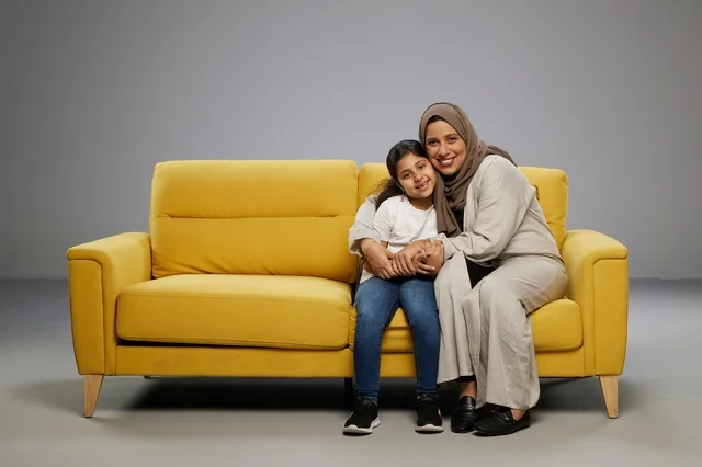 أم وابنتها تجلسان على أريكة صفراء في استوديو