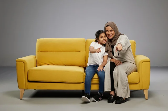 أم وابنتها تجلسان على أريكة صفراء وتشيران للأمام