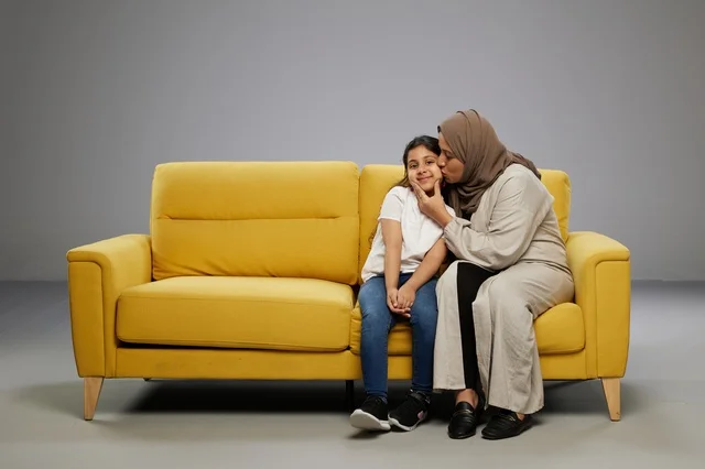 أم عربية تقبل ابنتها على أريكة صفراء