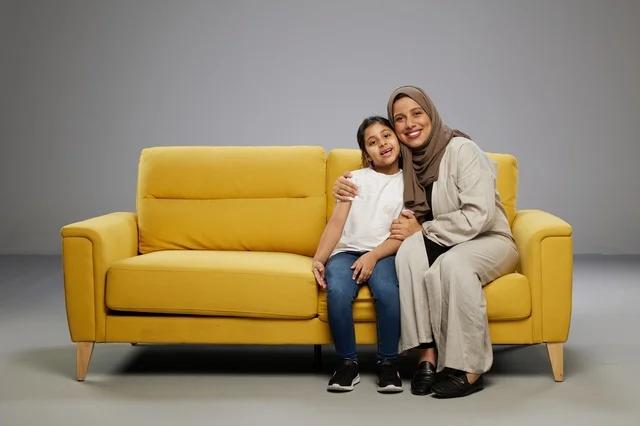 أم وابنتها تجلسان على أريكة صفراء في الاستوديو