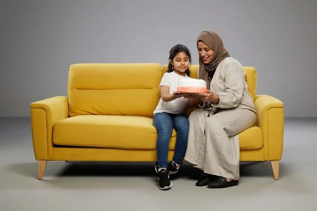 Arab Mother and Daughter with Cake on Yellow Sofa Studio