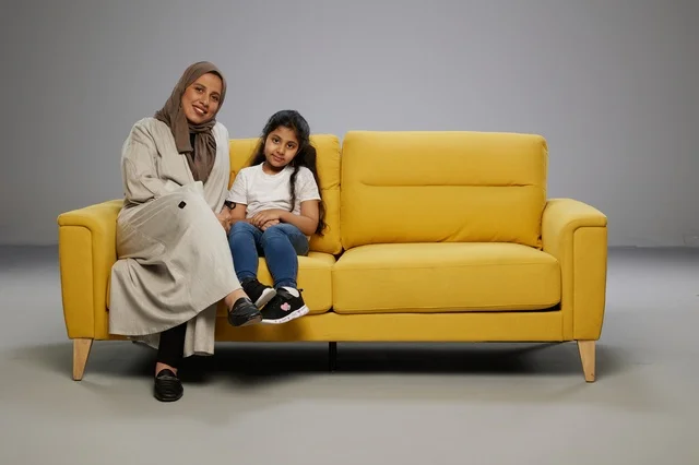 أم وابنتها تجلسان على أريكة صفراء في الاستوديو