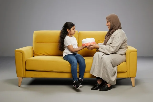 أم سعودية وابنتها مع كعكة على أريكة صفراء