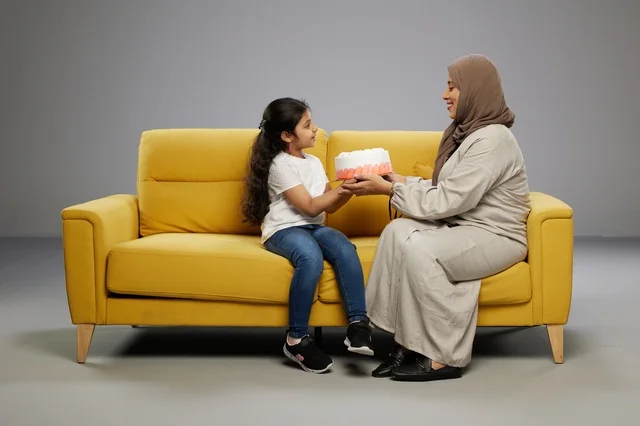 أم سعودية وابنتها مع كعكة على أريكة صفراء