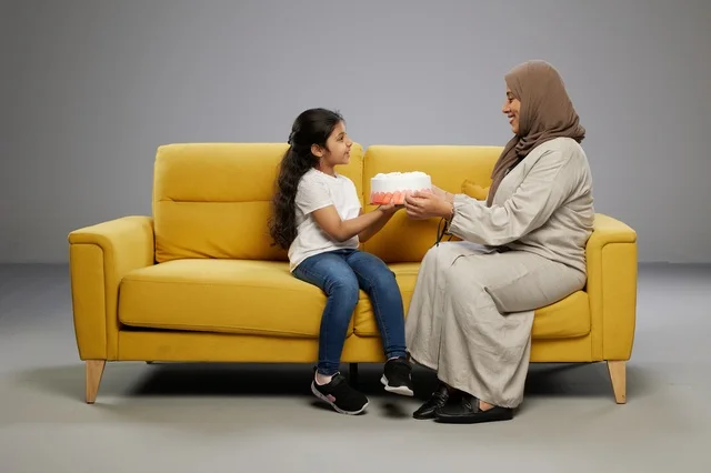 Arab Mother Surprises Daughter with Cake on Yellow Sofa