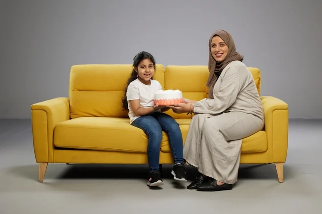 أم وابنتها مع كعكة على أريكة صفراء