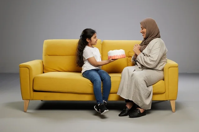 أم وابنتها مع كعكة عيد ميلاد على أريكة صفراء